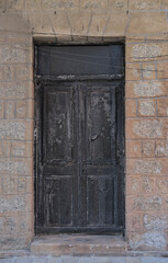 Close-up of an old black wooden door with cracked paint, set in a stone wall with textured bricks.