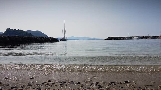 Static shot of sea waves and shoreline in Parga Greece. Gentle water movement, small pebbles and reflection of morning light create relaxing Mediterranean beach scene.