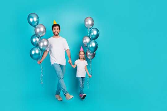Single father and daughter holding balloons and celebrating against a teal background in casual white shirts during a cheerful day