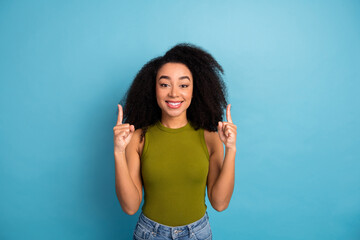 Fototapeta premium Smiling young woman in a green top making pointing gestures against a vibrant blue background