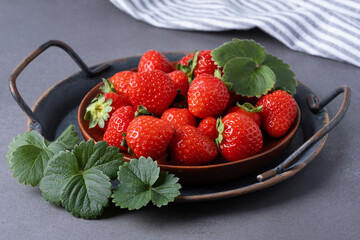 Freshly picked strawberries arranged neatly on a brown wooden plate with green leaves nearby