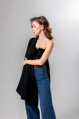 Young woman in stylish fashion pose wearing black top and jeans against simple backdrop