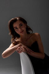 Fototapeta premium Woman with long hair poses gracefully on a white chair against a dark background in a studio setting