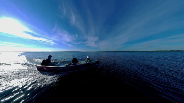 Boat with anglers tourists gliding during golden hour sunset with land skyline silhouetted. Best time for fishing game. View of sun set horizon at lake from boat. Cinematic view of evening leisure.