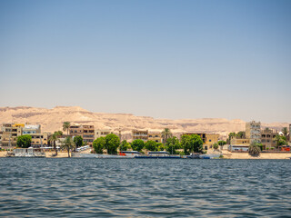 LUXOR, EGYPT : A panoramic view of Luxor’s city skyline along the Nile River, with sunlight reflecting on the water and the city’s historical architecture visible in the background.
