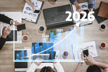 A diverse business team collaborates at a modern office desk, analyzing financial data with graphs projecting growth from 2023 to 2026. Tessel