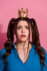 Young cheerful woman with long pigtails wearing a golden crown on a vibrant pink background expressing wonder