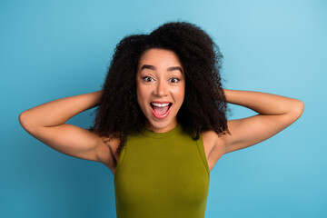 Excited young woman in green top expressing joy with a blue background, embodying happiness and...