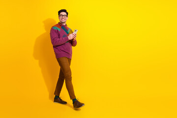 Confident young man in retro sweater using a smartphone against a vibrant yellow background