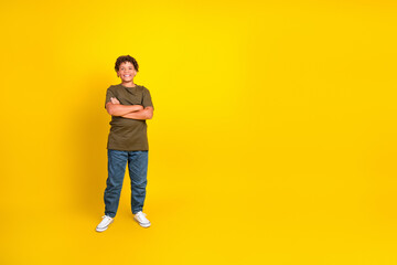 Fototapeta premium Funny confident young boy in casual khaki tshirt and jeans stands with arms crossed against a bright yellow background for a bold lifestyle promo