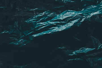 Wrinkled black plastic with a blue green light reflection. This abstract background features detailed folds and a glossy surface that is suitable for use as a background.