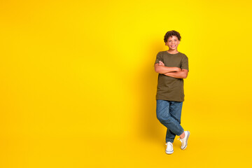 Funny stylish kid stands confidently on bright yellow background wearing olive t shirt jeans and white sneakers for a playful stock shot