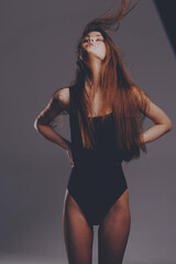 Young woman in black bodysuit posing confidently with flowing hair in studio lighting