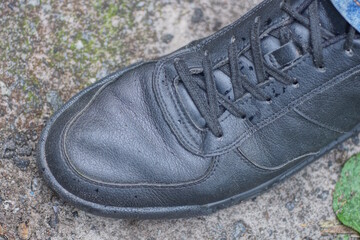 one leg in blue clothes and black leather boot stands on gray asphalt on city street