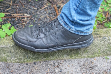 one leg in blue clothes and black leather boot stands on gray asphalt on city street