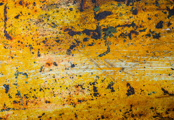 An abstract grunge texture background of an old metal surface. Faded and peeling yellow paint reveals the rust and scratches underneath, creating a worn, industrial pattern.