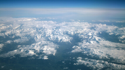 Aerial View Of Snowy Mountain Range With Clouds Over A Clear Blue Sky