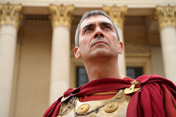 A Roman general, dressed in historical armor and a flowing cloak, stands confidently against grand columns in a public square under bright daylight. Generative AI.