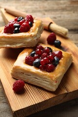 Tasty puff pastries with berries and brush on wooden table, closeup