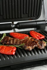 Electric grill with beef steaks, bell peppers and rosemary on white marble table, closeup