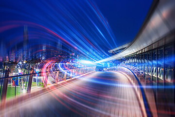 A creative nightscape of Hong Kong, China. Abstract streaks of light illuminate the elevated walkway against a dark sky, suggesting rapid transit and modern architecture. The creative composition show