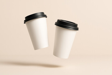 Two blank white disposable coffee cups with black lids floating in the air on a light neutral background studio shot