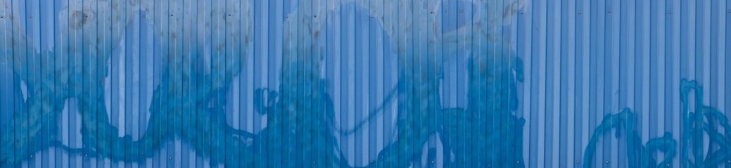 A textured blue metal corrugated fence wall background panorama with vertical stripes and a gradient effect, featuring abstract patterns and subtle variations in color
