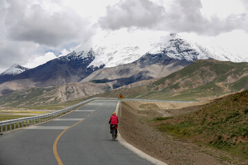 Cyclist riding on mountain road with snow-capped peaks in background