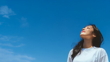 Korean female model posing happily on blue sky background. Wearing white t-shirt. Blank space for text.