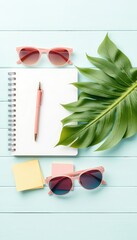 Planning a relaxing getaway A stylish notebook, sunglasses, notes, pen, and a lush leaf on a cool blue surface.