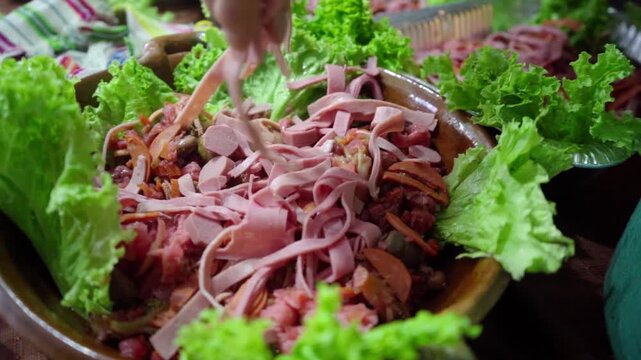 Detailed view of the final stage in preparing Guatemalan fiambre. Ham slices, red curtido, and lettuce leaves are arranged on a handcrafted clay plate, typical for All Saints&rsquo; Day.