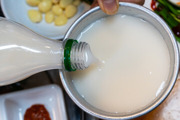 pouring makgeolli into the metal cup