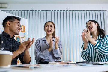 Three people are sitting at a table, working on a project. One of them is holding a piece of paper with a design on it. Scene is collaborative and focused
