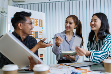 Three people are sitting at a table, working on a project. One of them is holding a piece of paper with a design on it. Scene is collaborative and focused
