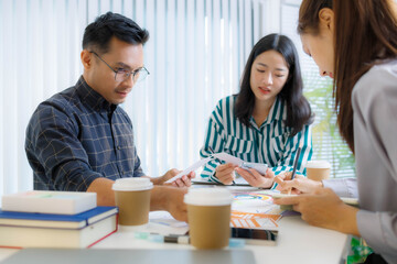 Obraz premium Three people are sitting at a table, working on a project. One of them is holding a piece of paper with a design on it. Scene is collaborative and focused 