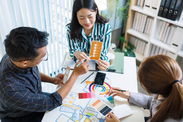 Three people are sitting at a table, working on a project. One of them is holding a piece of paper with a design on it. Scene is collaborative and focused
