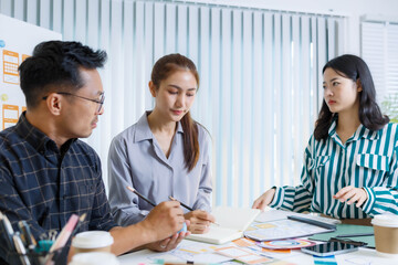 Obraz premium Three people are sitting at a table, working on a project. One of them is holding a piece of paper with a design on it. Scene is collaborative and focused 