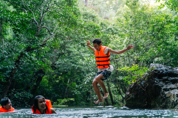Obraz premium Young Asian man and woman travel nature forest hiking and camping on summer holiday vacation. Generation z people friends enjoy and fun active lifestyle playing water in waterfall lagoon in sunny day.