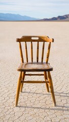 Wooden chair sits alone on cracked earth with mountains in the distance on a sunny day