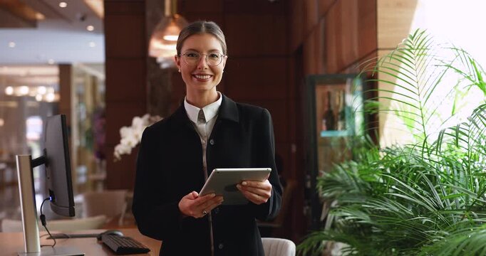 Smiling hotel receptionist with digital tablet posing at workplace