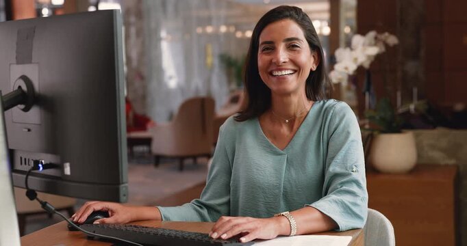 Hotel administrator or receptionist sits at desk working on pc