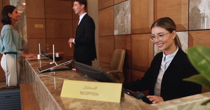 Hotel receptionist working on computer while colleague talks to guest