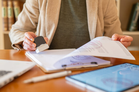 Person's hands holding a rubber stamp, making an official mark on a paper document on a clipboard, signifying approval and agreement in legal, banking, and real estate finance
