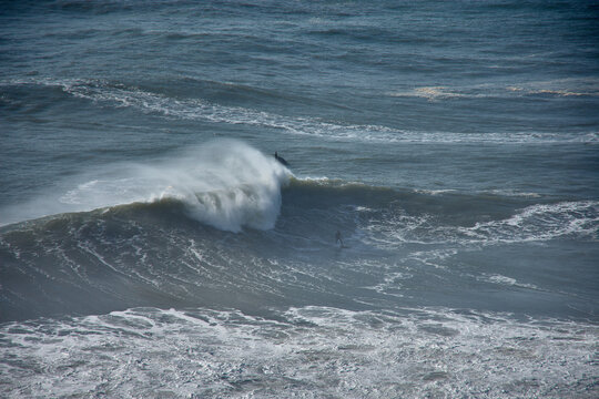 Panoramic view from the top of Nazare with surfers challenging the giant waves in a natural Atlantic setting in Portugal