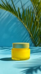 Bright yellow cream jar under a palm leaf shadow on a blue background, showcasing natural skincare and summer beauty essentials for a radiant complexion