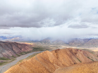 Aerial view over golden and red mountain ridges with low, heavy clouds and mist descending,...