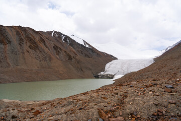 Ground-level view showing the face of a glacier and the pale green lake it feeds, with a rocky,...