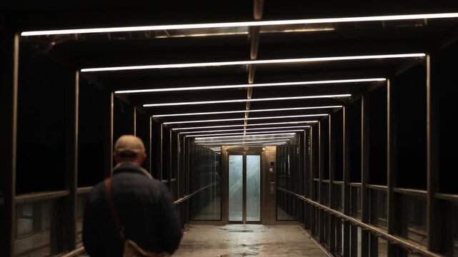 Stockholm, Sweden A man walks on a public elevated platform to an elevator on a rainy night in the Kvarnholmen district. 