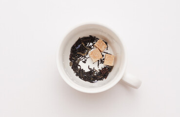 Cubes of cane sugar and black leaf tea in cup on white background. Top view