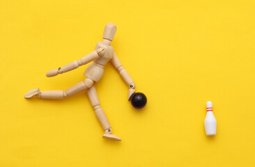 Wooden puppet playing miniature bowling on yellow background